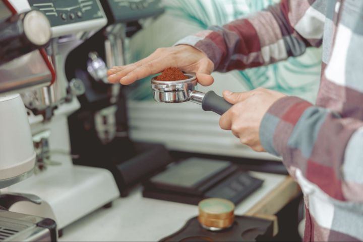 Barista holding an espresso machine part full of espresso grinds