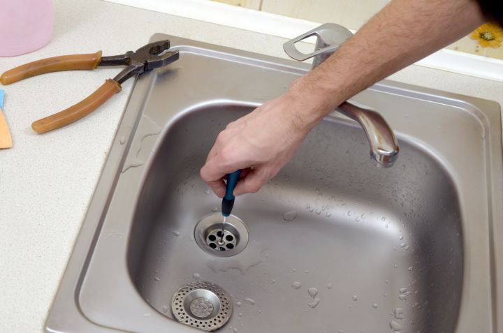 Someone using a screwdriver to remove a drain from a sink.