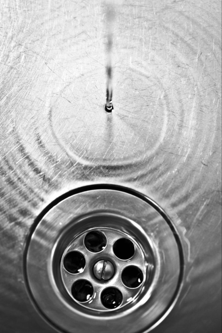 Closeup of a drain in a steel sink with water running in it