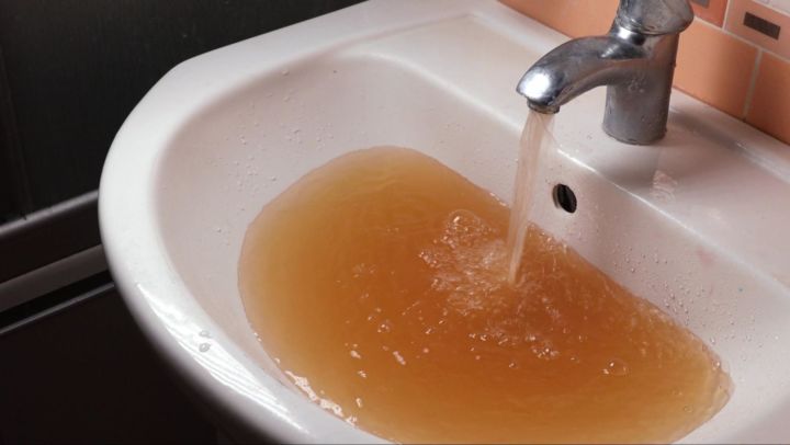 A white sink with dirty brown water running out of its faucet