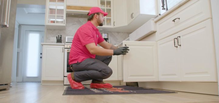 Uniformed Red Cap tech looking under a kitchen sink cabinet